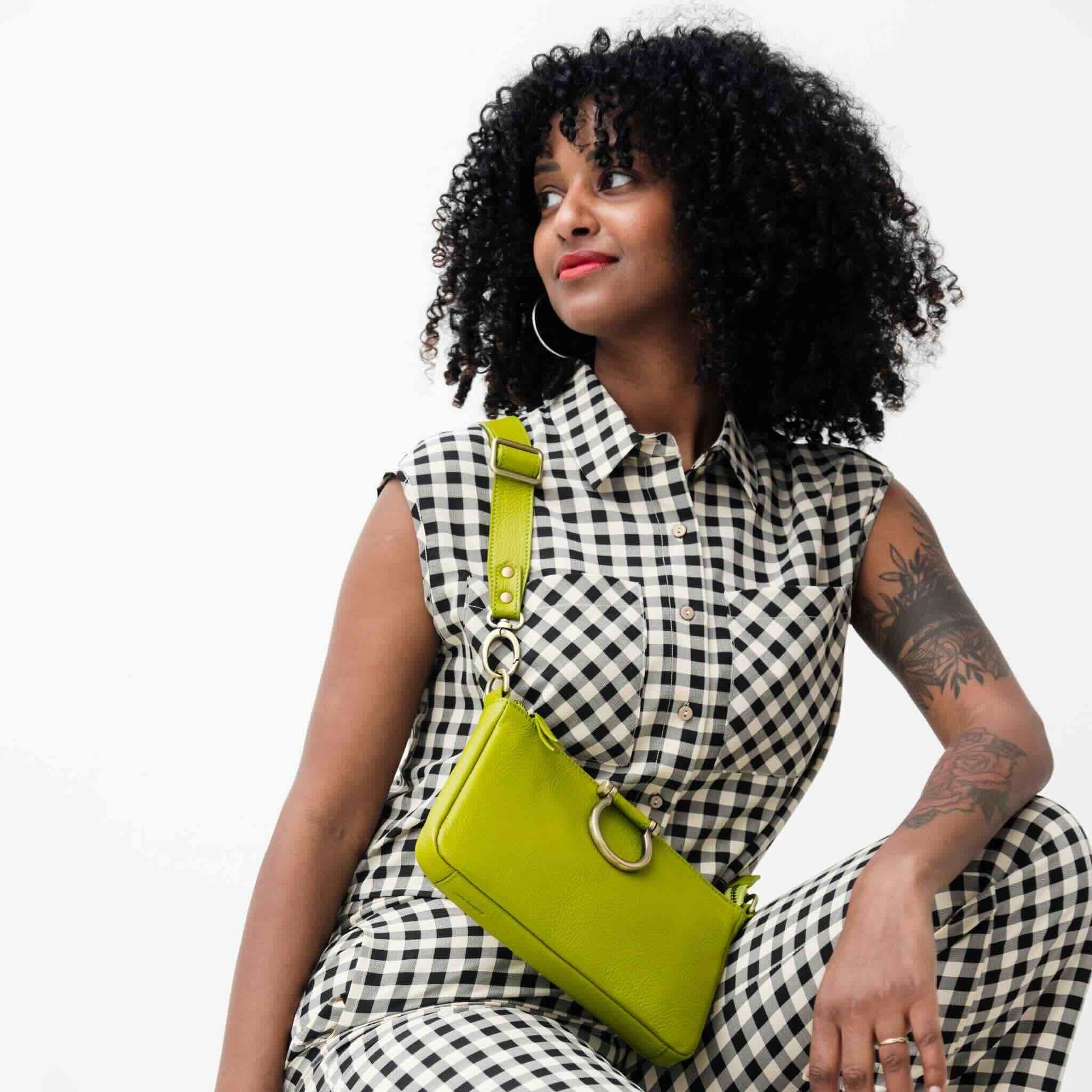 Woman in a black and white checkered dress with a green bag on a white background