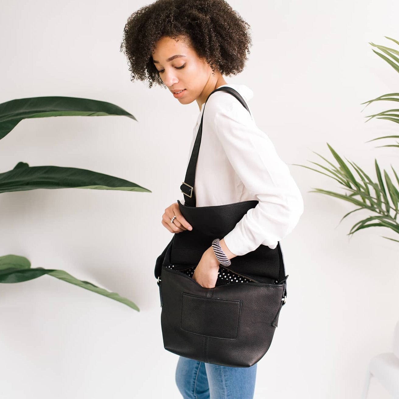 Lift the flap of the Rider crossbody bag in black raw leather to expose its main zippered compartment and exterior slip pocket.