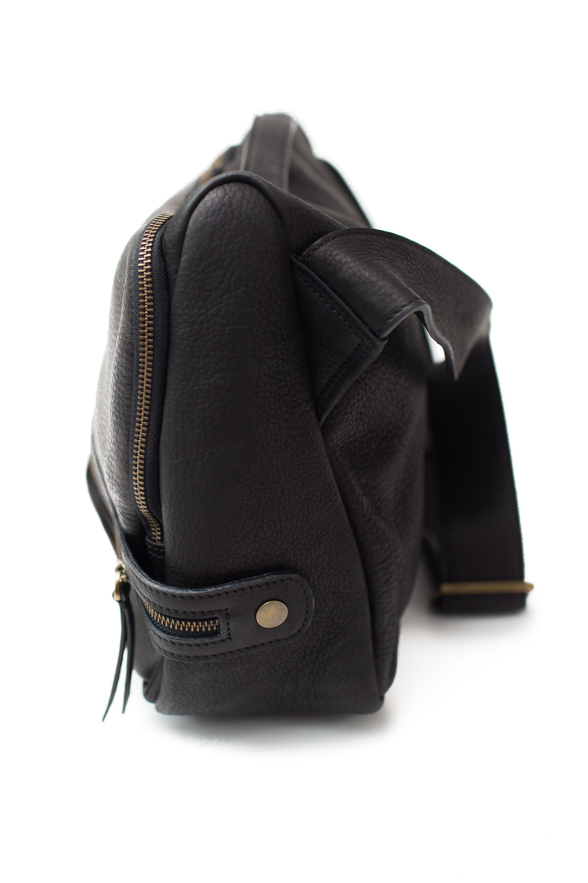 The side profile of the Rapinoe unisex messenger bag in black raw leather is clean and classic.