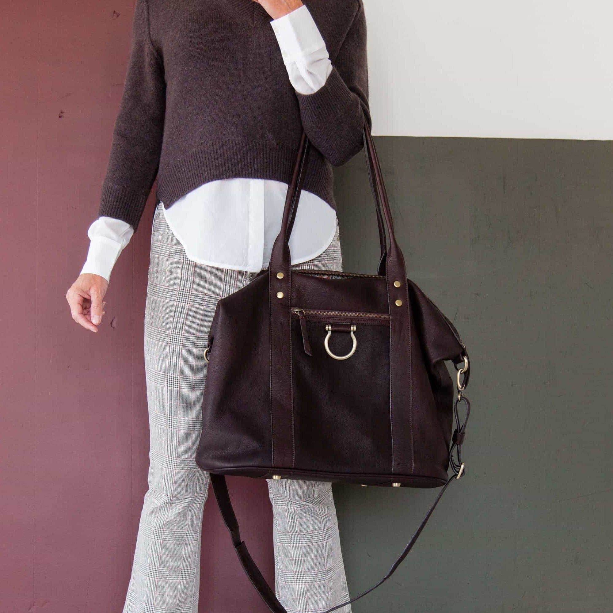 Hold the So Honey weekender tote in chocolate brown raw leather by the top handles.
